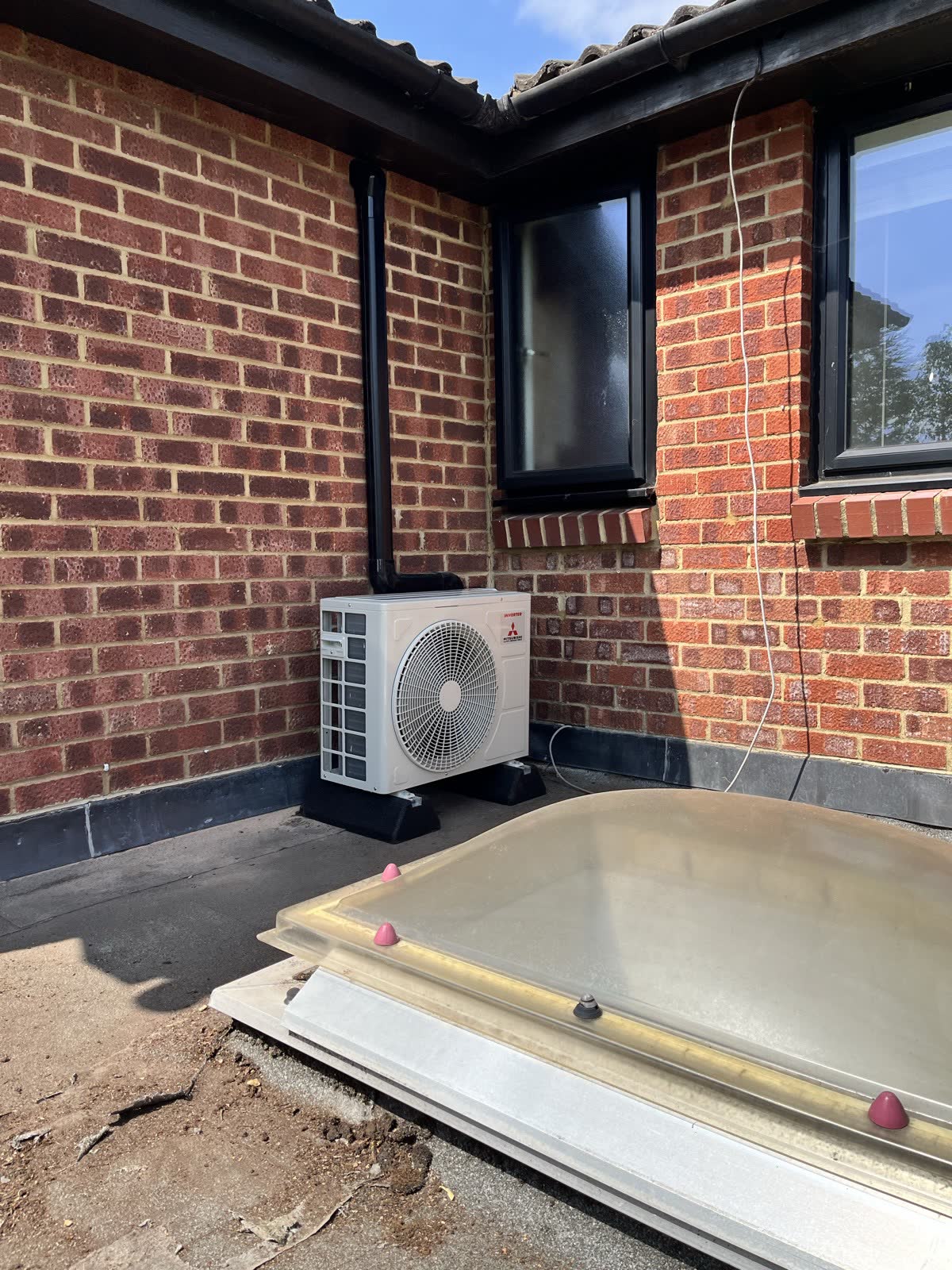 An outdoor air conditioning unit with black trunking run to follow the existing downpipe